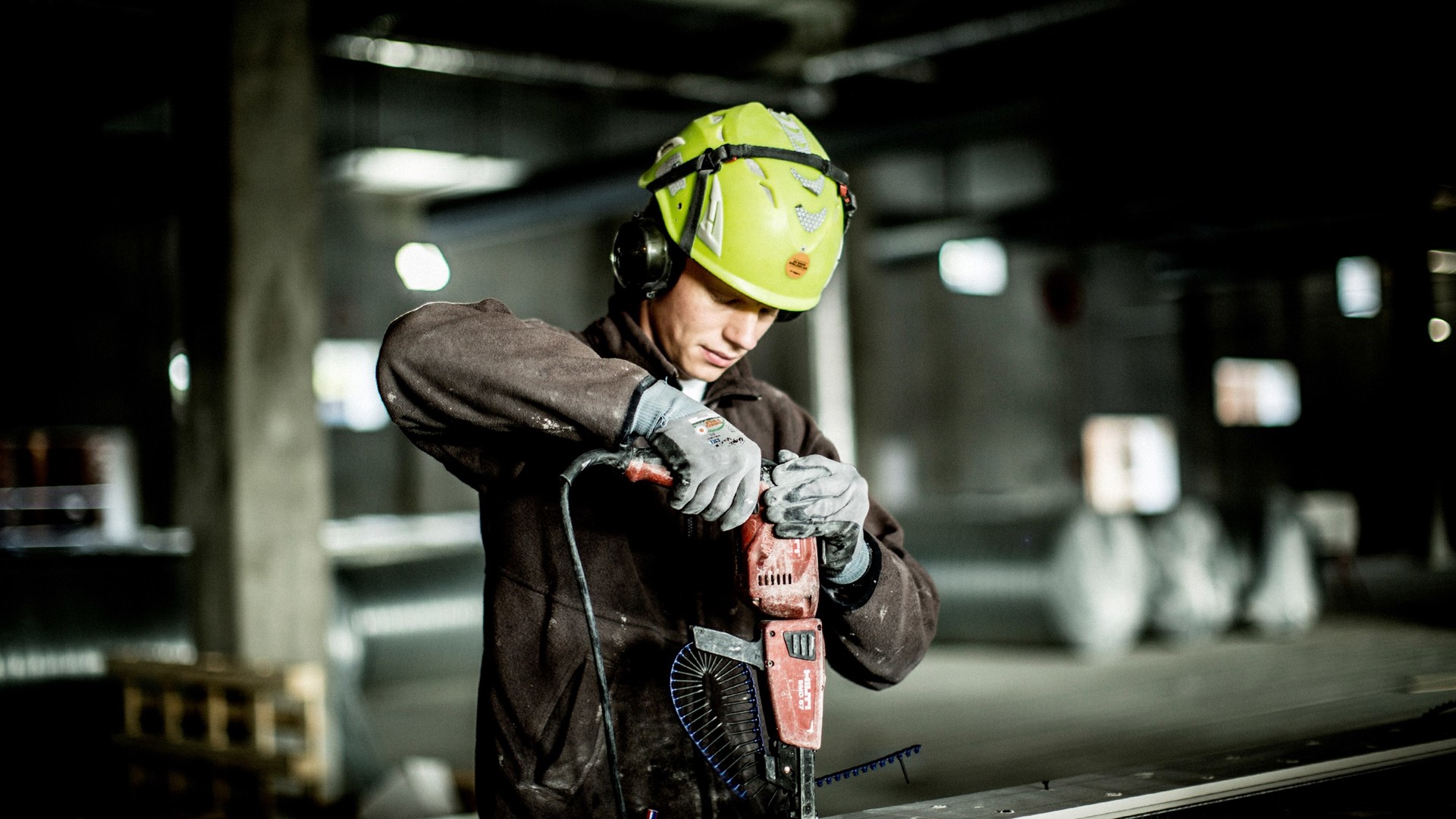 Mand der er ved at bore i metal. Han er udstyret med hjelm og arbejdstøj.